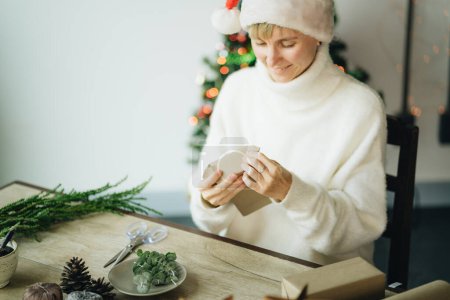 Téléchargez les photos : Chapeau femme en Santa enveloppant cadeaux de Noël avec des matériaux écologiques à la maison - en image libre de droit