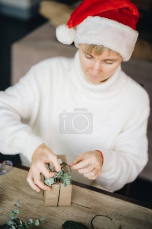 Téléchargez les photos : Chapeau femme en Santa enveloppant cadeaux de Noël avec des matériaux écologiques à la maison - en image libre de droit