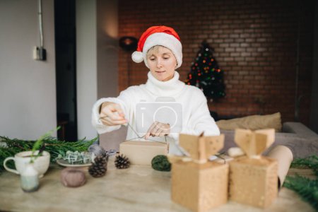 Foto de Mujer en Santa sombrero de envolver regalos de Navidad con materiales ecológicos en casa - Imagen libre de derechos