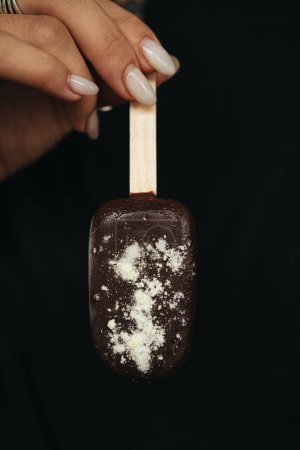 mano femenina está sosteniendo un helado esquimal en el fondo oscuro. Foto de alta calidad