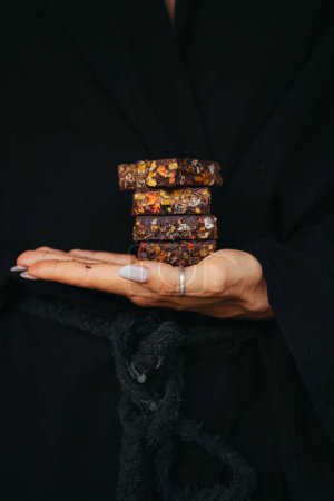 Weibliche Hände halten Schokoriegel mit Nüssen und Früchten vor schwarzem Hintergrund. Hochwertiges Foto