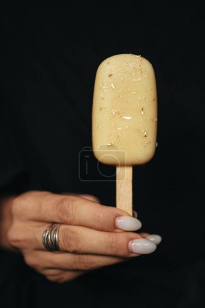 main féminine tient un eskimo de crème glacée à fond sombre. Photo de haute qualité