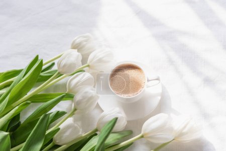 Téléchargez les photos : Tasse à café confortable le matin avec des fleurs de tulipes blanches d'en haut, petit déjeuner sur la fête des mères ou la journée des femmes. Vue du dessus avec espace de copie Composition florale Fond romantique - en image libre de droit
