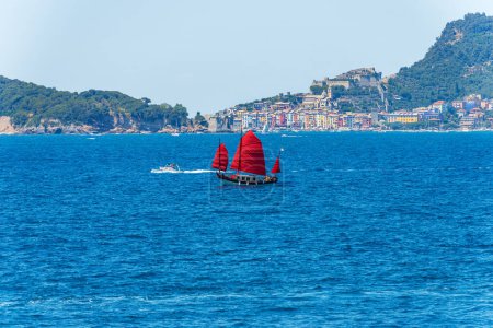 Photo for Old sailboat with three red sails in the blue Mediterranean sea in front of the famous Porto Venere or Portovenere town, UNESCO world heritage site, Gulf of La Spezia, Liguria, Italy, Europe. - Royalty Free Image