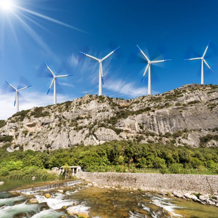 Photo for Group of white and blue wind turbines on the top of a mountain landscape, blue sky with clouds on background, river with rapids in the foreground. - Royalty Free Image