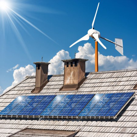 Solar panels and a small wind turbine on the top of a wooden roof of a house, against a clear blue sky with clouds and sunbeams. Renewable energy concept.