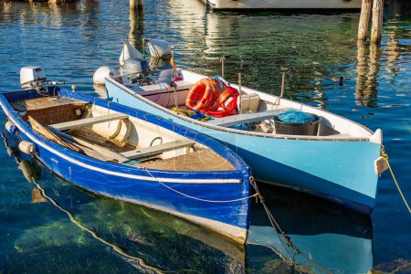 Foto de Primer plano de dos pequeños barcos pesqueros de madera amarrados en el pequeño puerto del pueblo de Malcesine, complejo turístico en la costa del lago de Garda. Verona provincia, Véneto, Italia, sur de Europa. - Imagen libre de derechos