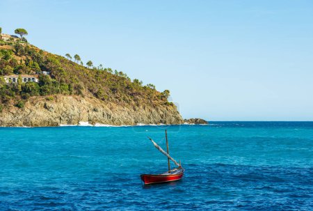Foto de Costa rocosa y paisaje marino con un pequeño velero de madera amarrado frente al pequeño pueblo de Bonassola, Mar Mediterráneo, provincia de La Spezia, Liguria, Italia, sur de Europa. - Imagen libre de derechos