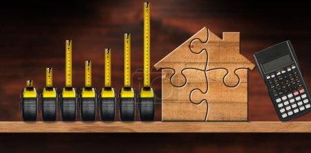 Foto de Grupo de siete medidas de cinta que forman un gráfico de barras, en un estante de madera con una casa modelo de madera hecha de piezas de rompecabezas y una calculadora. - Imagen libre de derechos