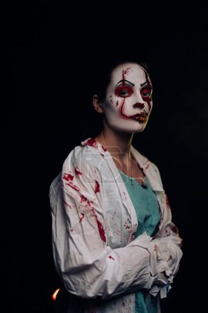 Téléchargez les photos : Jeune femme dépeint zombie assoiffé de sang avec des blessures horribles sur le visage et des vêtements sanglants sur fond sombre. Image effrayante pour Halloween. - en image libre de droit