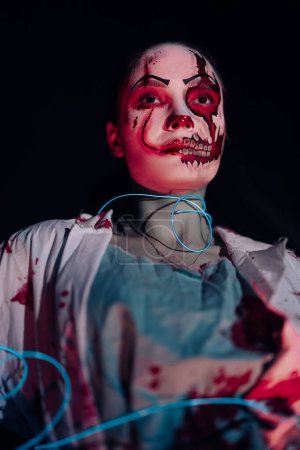 Foto de Una joven con una banda azul brillante retrata a un zombi sediento de sangre con heridas en la cara y dientes de horror contra un fondo oscuro. Imagen aterradora para Halloween. Retrato. - Imagen libre de derechos