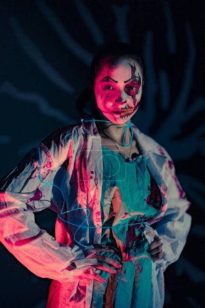 Foto de Una joven con una banda azul brillante retrata a un zombi sediento de sangre con heridas en su cara contra un fondo oscuro. Imagen aterradora para Halloween. - Imagen libre de derechos