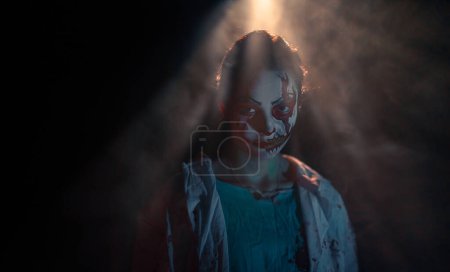 Téléchargez les photos : Jeune femme dépeint zombie sanguinaire avec des blessures horribles sur le visage et des vêtements sanglants sur fond sombre sous la lumière. Image effrayante pour Halloween. Portrait. - en image libre de droit