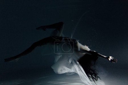 Photo for Underwater shoot of beautiful woman in white flying transparent dress dancing in water in sunbeams. Fantasy mermaid against water surface background with rays of lights. - Royalty Free Image