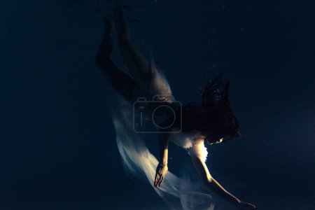 Photo for Underwater shoot of beautiful woman in white flying transparent dress swimming in water through sunbeams. Fantasy mermaid against water surface background with rays of lights. - Royalty Free Image