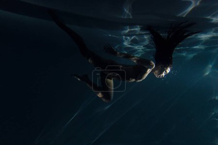 Photo for Underwater shoot of beautiful woman with long hair dancing in water in sunbeams. Fantasy mermaid against water surface background with rays of lights. - Royalty Free Image