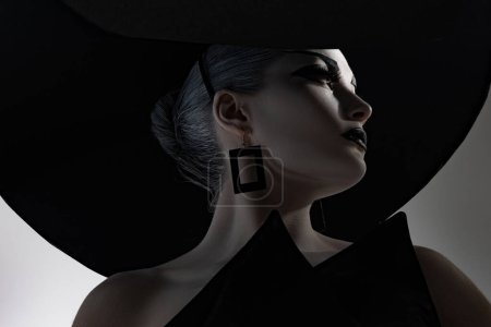 Foto de Retrato de mujer joven en elegante sombrero de ala ancha, pendientes y vestido negro. Vista inferior. - Imagen libre de derechos