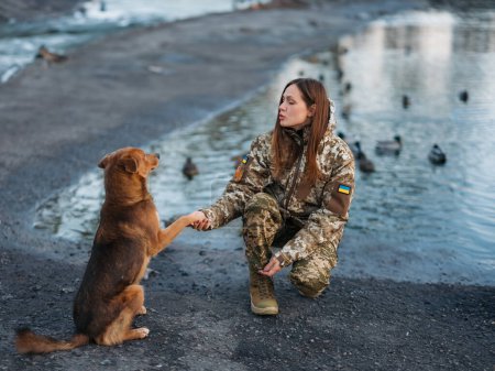 Foto de Mujer soldado ucraniano descansando en el parque con el perro en vacaciones. Mujeres y guerra. Guerra en Ucrania. Invasión militar rusa. Traducción del ucraniano: Fuerzas Armadas de Ucrania, apellido. - Imagen libre de derechos
