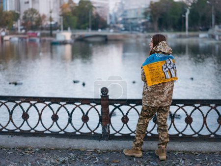 Foto de Mujer soldado ucraniana sosteniendo bandera con firmas de guerreros ucranianos y descansando en el parque de vacaciones. Traducción del ucraniano: Gloria a Ucrania. - Imagen libre de derechos