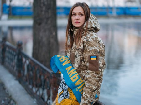 Foto de Mujer soldado ucraniana sosteniendo bandera con firmas de guerreros ucranianos y descansando en el parque de vacaciones. Traducción del ucraniano: Fuerzas Armadas de Ucrania, Gloria a Ucrania, apellido. - Imagen libre de derechos