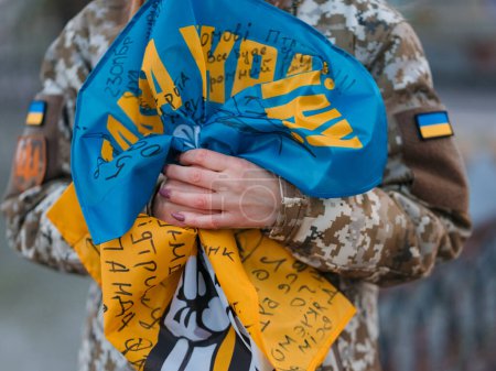 Foto de Mujer soldado ucraniana sosteniendo bandera con firmas de guerreros ucranianos y descansando en el parque de vacaciones. Traducción del ucraniano: Gloria a Ucrania. Primer plano.. - Imagen libre de derechos