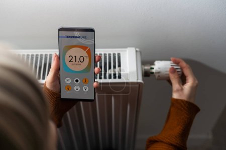 Foto de Smartphone con aplicación lanzada para ajuste de temperatura del aire frente al radiador. Microclima de salud en el hogar. - Imagen libre de derechos