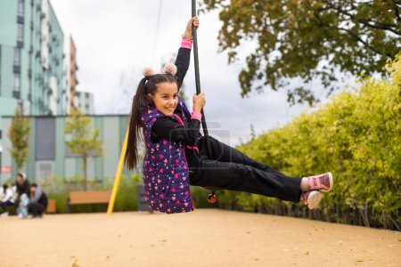 Photo for Smiling little girl swinging on a rope at a playground. - Royalty Free Image