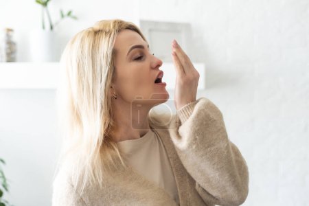 Gesundheitswesen: Frau kontrolliert ihren Atem mit der Hand Nahaufnahme Porträt Kopfschuss schläfrige junge Frau mit weit geöffnetem Mund