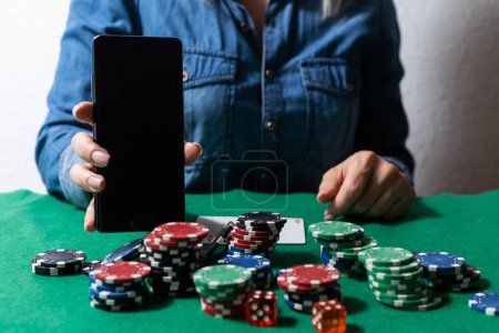 joueur de poker en ligne avec un smartphone à une table de casino avec des cartes et des jetons