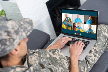 Téléchargez les photos : Jeune soldat en uniforme militaire parlant à quelqu'un tout en ayant une conversation vidéo sur ordinateur. - en image libre de droit