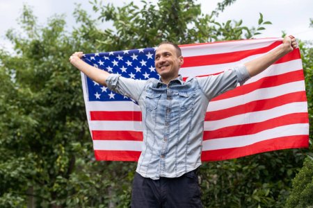 Photo for Attractive man holding Flag of the United States on blue sky background on a clear, sunny day. View from the back, close-up. National holiday concept. High quality photo - Royalty Free Image