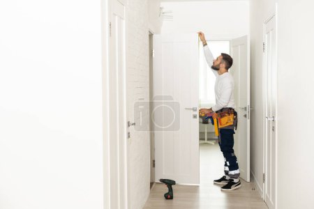 Foto de Good looking man working as handyman and fixing a door lock in a house entrance. - Imagen libre de derechos