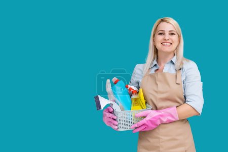 Photo for Photo of caucasian pretty housemaid wearing rubber gloves for hands protection holding bucket with cleaning supplies isolated over blue background. - Royalty Free Image