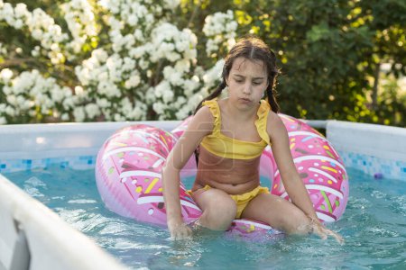 Feliz niña jugando con el anillo inflable colorido en la piscina al aire libre en el día caliente del verano. Los niños aprenden a nadar. Juguetes de agua infantil. Los niños juegan en el resort tropical. Vacaciones familiares en playa.