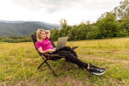 Photo for Young business woman working at the computer on the rock. Young girl downshifter working at a laptop at sunset or sunrise on the top of the mountain, working day - Royalty Free Image