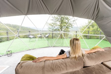 Téléchargez les photos : Une femme assise dans une tente de glamping géo dôme, regarde la nature - en image libre de droit