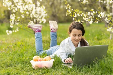 Foto de Little girl using laptop computer in a backyard. Child studying at home doing her homework or having online lesson. Homeschooling concept - Imagen libre de derechos