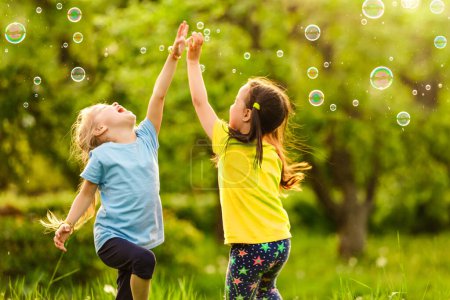 Photo for Two little girls are blowing soap bubbles, outdoor shoot - Royalty Free Image