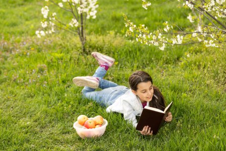 Téléchargez les photos : Petite fille avec une bible dans le jardin, priant, rêvant à l'extérieur - en image libre de droit