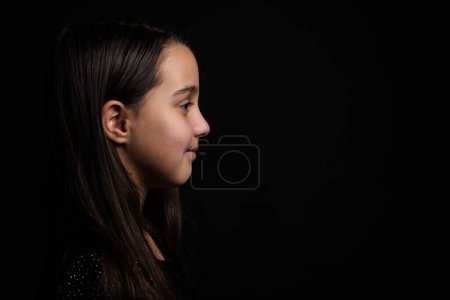 Photo for Profile side view face brown-haired little girl standing isolated on black studio background. - Royalty Free Image