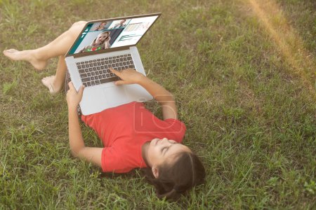 Foto de Niña aprende, un adolescente que trabaja en un ordenador portátil acostado en un prado. Internet móvil en las zonas rurales. educación a distancia
. - Imagen libre de derechos