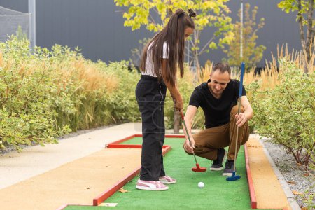 father and daughter playing mini golf together in the park.