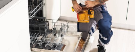 Photo for Closeup repair and installation of dishwasher, male worker with tool in uniform - Royalty Free Image