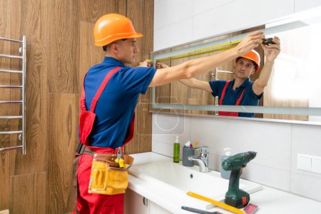 Téléchargez les photos : Male repairman hangs the modern electronic bathroom mirror. accessories and furniture for bathrooms and houses. - en image libre de droit