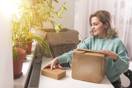 Closeup view of female online store small business owner seller entrepreneur packing package post shipping box preparing delivery parcel on table. Ecommerce dropshipping shipment service concept.