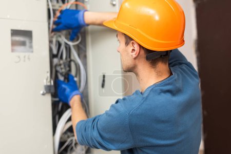 Photo for Close up shot of hand of aged electrician repairman in uniform working, fixing, installing ethernet cable in fuse box, holding flashlight and cable. hand and cable. - Royalty Free Image