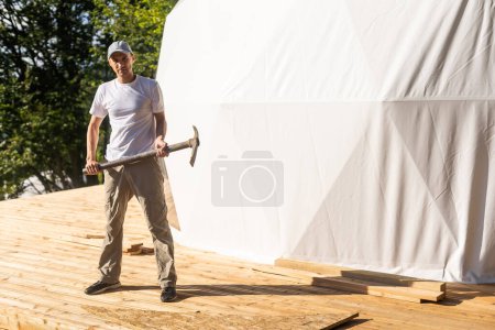 Téléchargez les photos : The master builds the dome. Outside spherical glamping dome. Hemispherical structure lattice shell geodesic polyhedron. Camping house hotel party tent - en image libre de droit