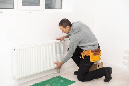 Téléchargez les photos : Repairman using tools while installing or repairing heating radiator. plumber installing heating system in apartment. radiator installation, plumbing works and home renovation. - en image libre de droit