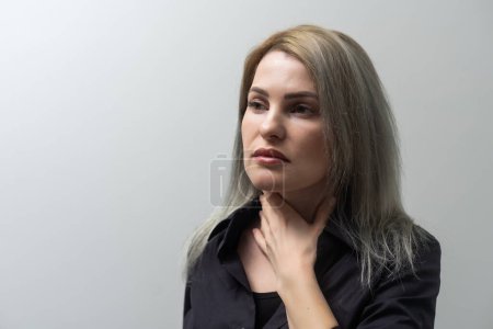 Closeup of sick woman having sore throat, tonsillitis, feeling sick, caught cold, suffering from painful swallowing, strong pain in throat, holding hand on her neck, isolated on studio light