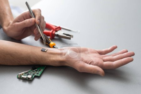 Robot arm concept. Man shows biomechanical prosthetic hand. Guy repairs his hand with tool. Bioengineering, transhumanism, biohacking, human cyborg. Fusion of electronics, mechanics and the human body